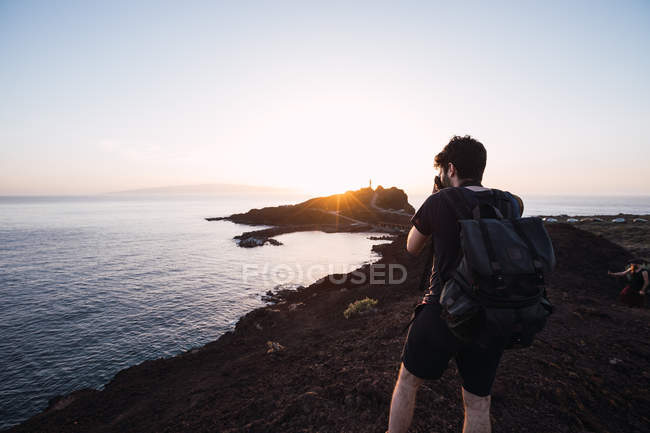 Fotógrafo masculino imaginando puesta de sol sobre costa remota - foto de stock