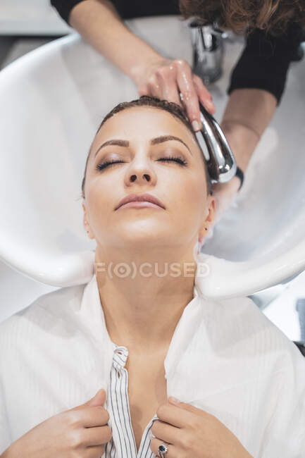Styliste lavage des cheveux à jeune femme — Photo de stock