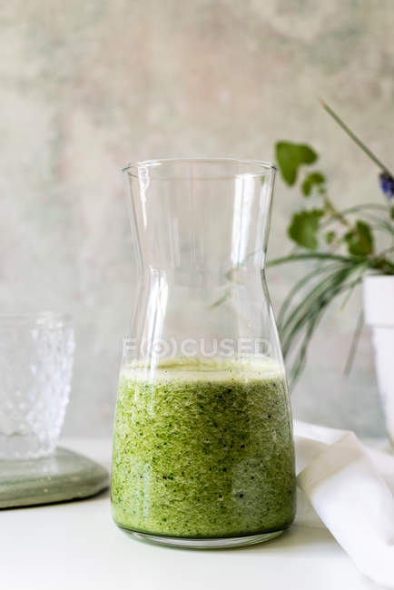 Frullato verde sano di spinaci, avocado e kiwi, mela e limone in brocca sul tavolo bianco — Foto stock