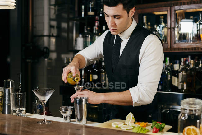 Junger eleganter Barmann, der hinter einer Theke Getränke mit Früchten mixt — Stockfoto