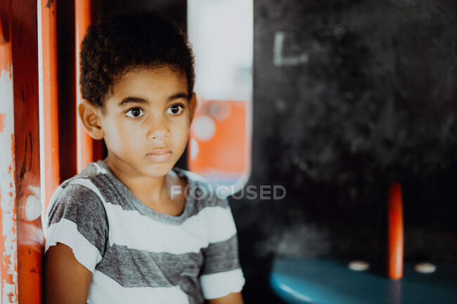 Мрійливий афроамериканець у смугастій футболці, що дивиться убік, сидячи всередині будинку на дитячому майданчику. — стокове фото