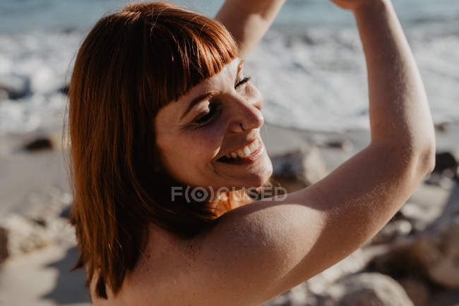 Вид збоку доросла жінка тримає очі закритими і весело посміхається під час танців на березі моря в сонячний день на природі — стокове фото