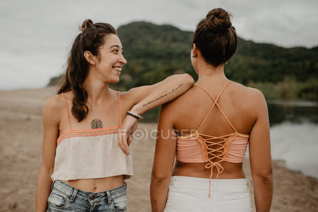 Woman with tattooed arm leaning on shoulder of unrecognizable friend while spending time on beach together — Stock Photo