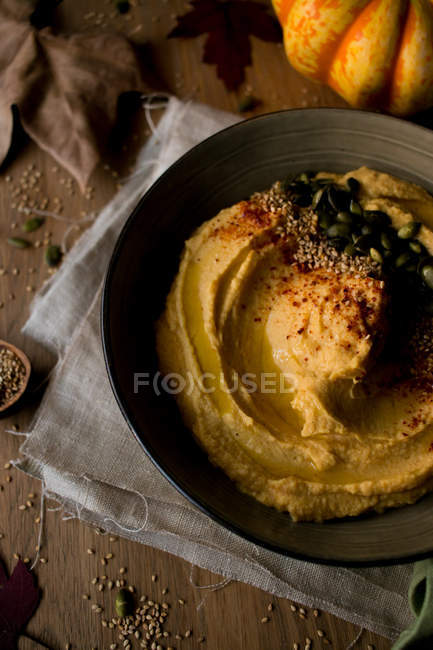 Set of yummy pumpkin hummus with seeds on cloth napkin placed on lumber tabletop with dried autumn leaves — Stock Photo
