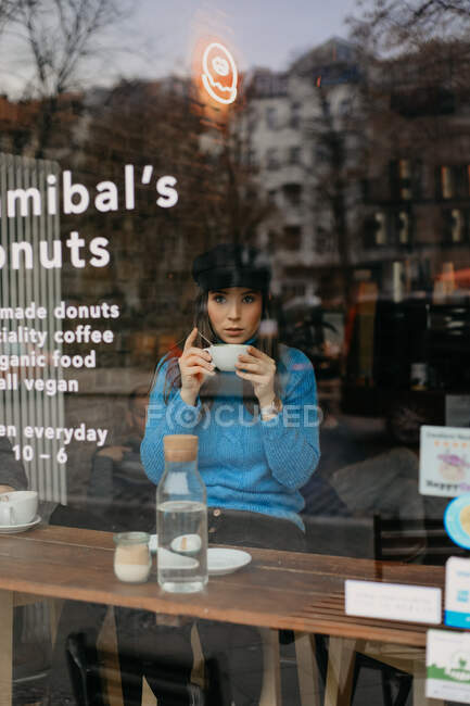From outside, photo of stylish woman drinking coffee into a coffee shop looking away — Stock Photo