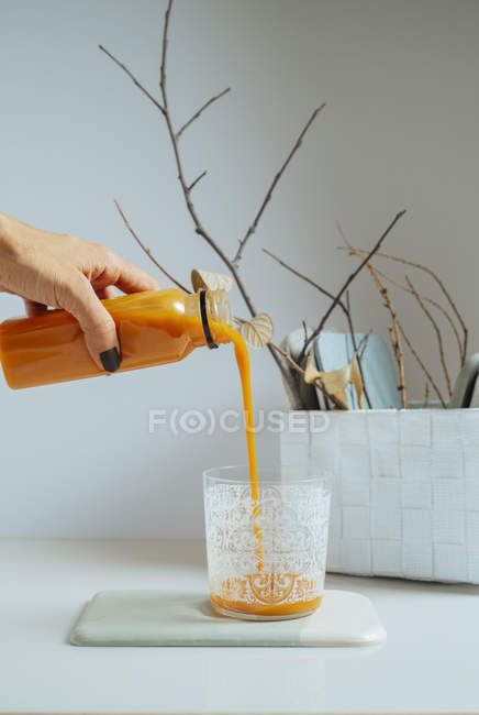 Mano femenina sirviendo batido de mango fresco en vaso sobre mesa blanca - foto de stock