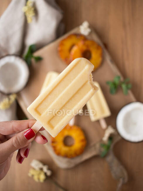 Рука анонимной женщины держит кокосовое и ананасовое мороженое над размытым столом — стоковое фото