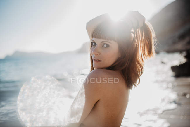 Spots of bright sunlight in front of naked woman looking at camera posing against cloudless sky in nature — Stock Photo