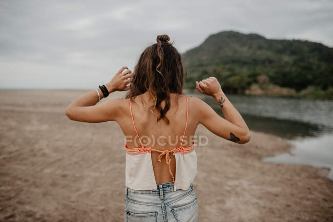 Back view of young female in casual outfit standing on sandy beach towards sea during sundown in nature — Stock Photo