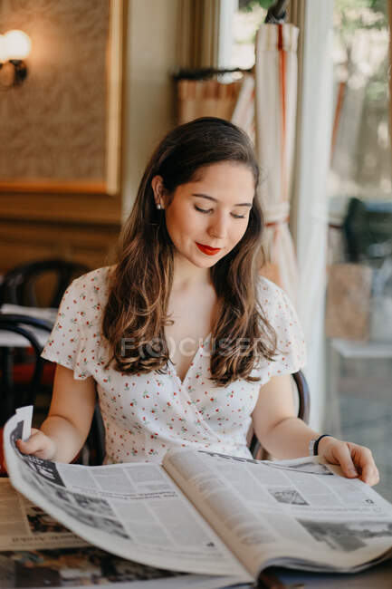Joven bonita dama leyendo un periódico en una cafetería vintage - foto de stock