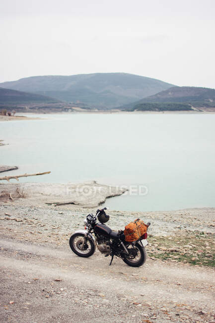Мотоцикл припаркован на сельской дороге на берегу спокойного озера во время поездки на природу — стоковое фото