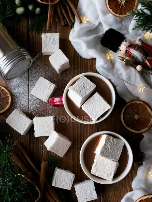 Aromatische Zimtstangen und getrocknete Zitrusfrüchte auf einer Holztischplatte neben Tassen mit leckerer heißer Schokolade mit weichen Marshmallows und verschiedenen Weihnachtsdekorationen — Stockfoto