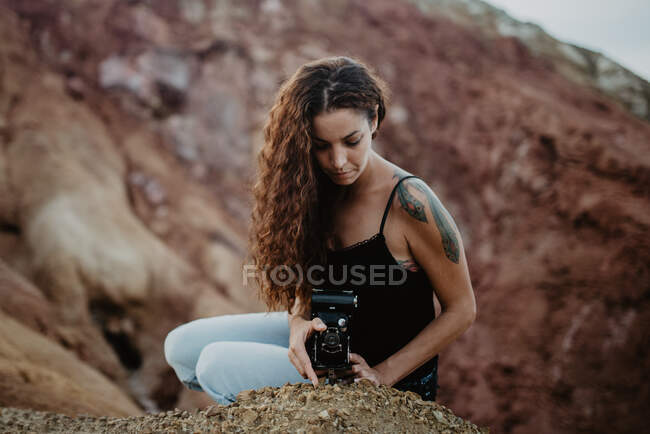 Feminino viajante com câmera vintage sentado em penhasco rochoso áspero na natureza — Fotografia de Stock