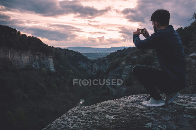 Man with photo camera sitting on hill mountain with magnificent sunset — Stock Photo