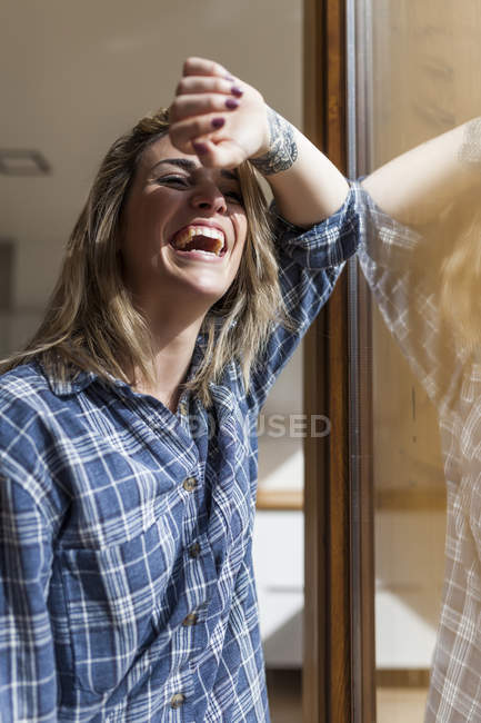 Schöne junge Frau an einem Fenster ihres Hauses lachend — Stockfoto