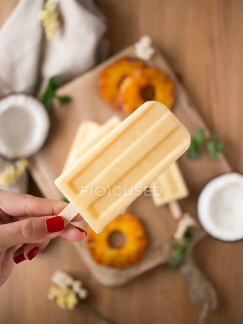 Mano di anonima femmina che tiene il cocco e il gelato all'ananas sul tavolo sfocato — Foto stock