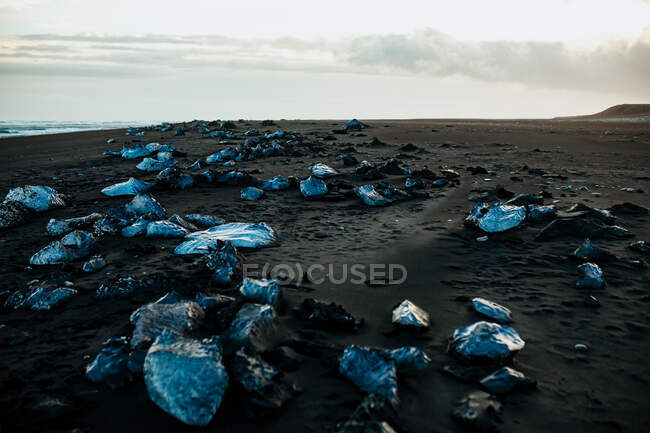 Rocce grezze situate sulla costa sabbiosa vicino al mare contro nuvoloso cielo mattutino in natura — Foto stock