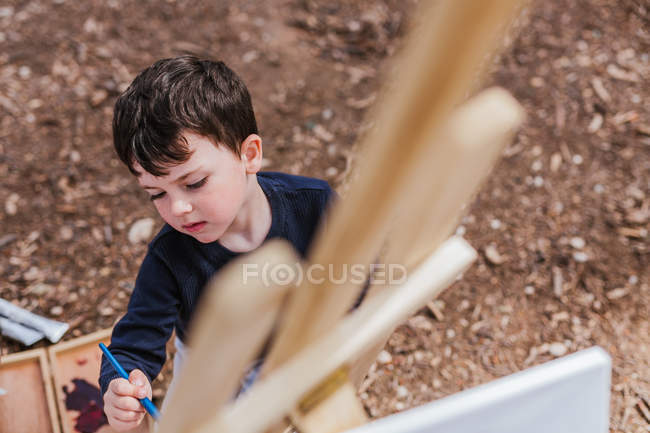 Boy painting on easel in countryside — Stock Photo