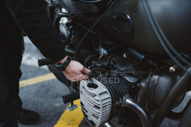 Anonymous male fixing engine of motorbike on parking lot on city street — Stock Photo