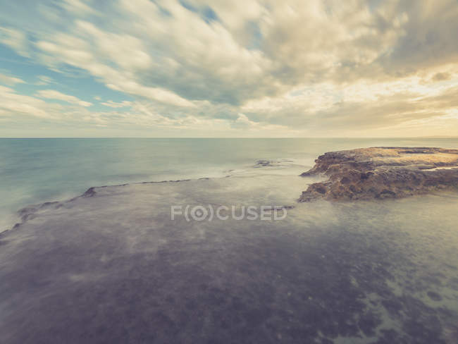 Costa rocciosa e mare azzurro sullo sfondo del cielo con nuvole — Foto stock