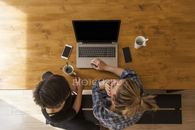 Dos mujeres hermosas y jóvenes desayunando en casa y usando el portátil - foto de stock