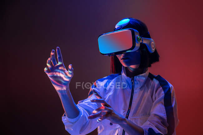 Aufgeregte junge Frau berührt Luft, während sie Virtual-Reality-Erfahrung im Neonlicht hat — Stockfoto