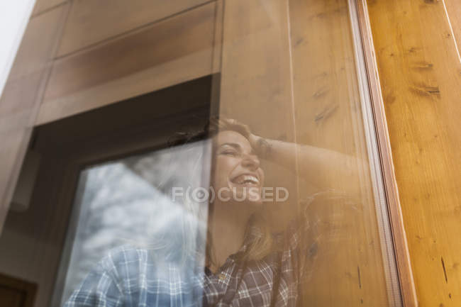 Schöne und junge Frau reflektiert in einem Fenster ihres Hauses und lächelt — Stockfoto
