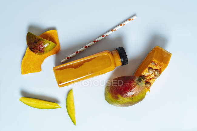 Smoothie végétalien à la mangue et à la citrouille en bouteille sur fond blanc avec ingrédients — Photo de stock