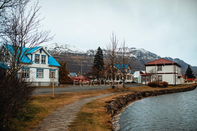 Lovely cottages located on shore of calm sea near snowy mountain ridge on gray day in coastal town — Stock Photo