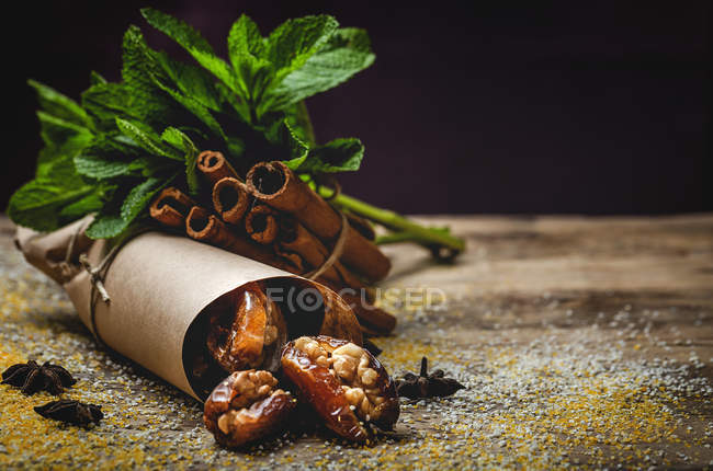 Getrocknete Datteln, Feigen, frische Minze und Zimt als Halal-Snack für Ramadan, eingewickelt in Pergament auf Holztisch — Stockfoto
