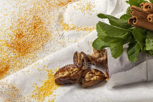 Snack halal para Ramadán con dátiles secos, higos, menta fresca y canela sobre tela blanca - foto de stock