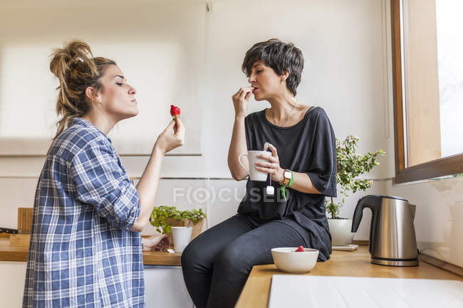 Zwei schöne junge Frauen, die zu Hause frühstücken und Spaß haben, auf der Küche sitzen — Stockfoto