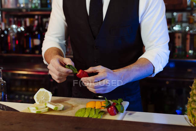 Crop joven barman elegante anónimo trabajando detrás de un mostrador de bar preparando frutas para bebidas de cóctel - foto de stock