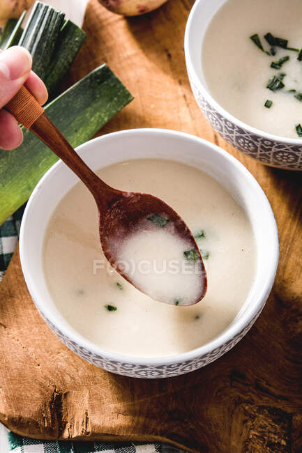 Atire de cima da mão de colheita com colher e sopa Vichyssoise saborosa na mesa de madeira com alho-poró — Fotografia de Stock