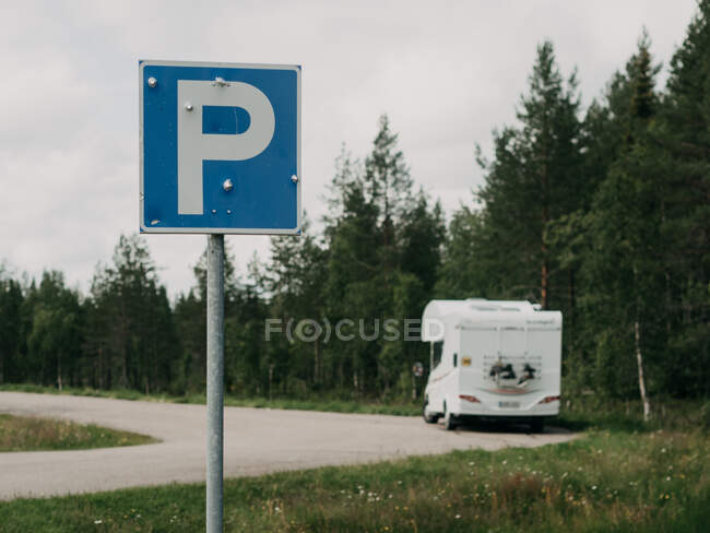 White camper car standing near parking sign at bent of road in forest in summer day — Stock Photo