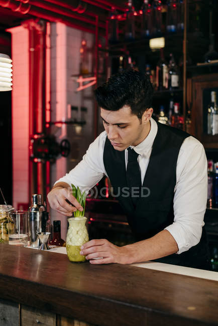 Jovem barman elegante trabalhando atrás de um balcão de bar preparando bebida em um copo — Fotografia de Stock