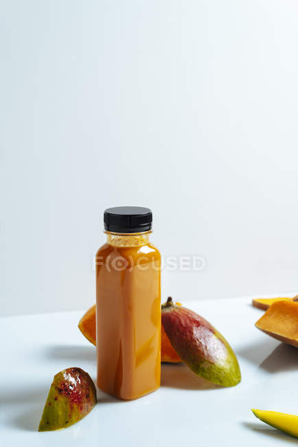 Frullato vegano di mango e zucca in bottiglia su fondo bianco con ingredienti — Foto stock