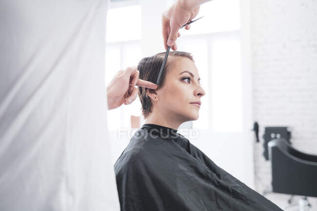 Cabeleireiro corta o cabelo da mulher com tesoura — Fotografia de Stock