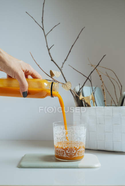 Женская рука, подающая свежий коктейль манго в стекло на белом столе — стоковое фото