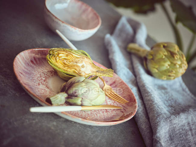 Alcachofa fresca a la mitad en placa de cerámica rosa en la mesa - foto de stock