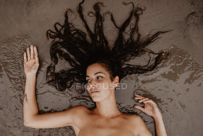 Mulher nua deitada na areia molhada na praia — Fotografia de Stock
