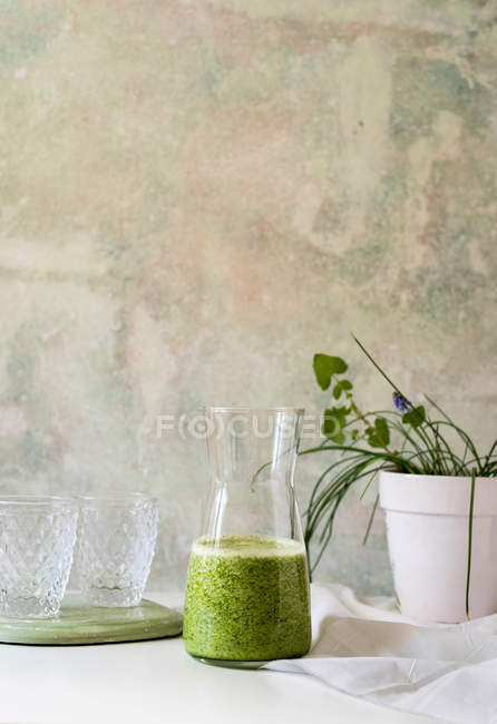 Healthy green smoothie of spinach, avocado and kiwi, apple and lemon in jug on white table — Stock Photo