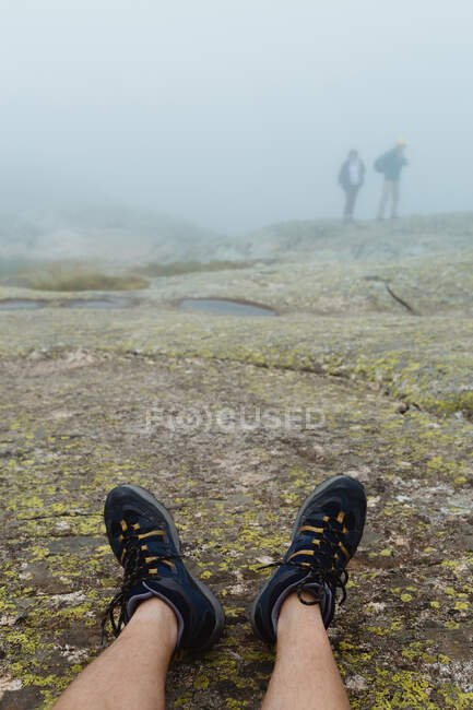 Gambe di un viaggiatore anonimo sdraiato su un terreno roccioso in una giornata nebbiosa in una campagna maestosa — Foto stock