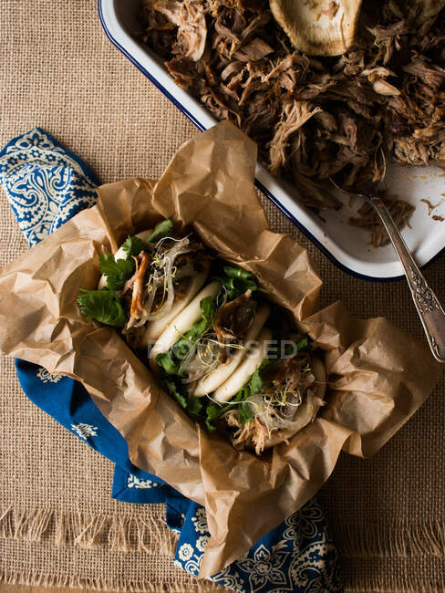 Metal bowl with delicious pulled pork and fresh bao bun placed on ornamental and linen napkins — Stock Photo