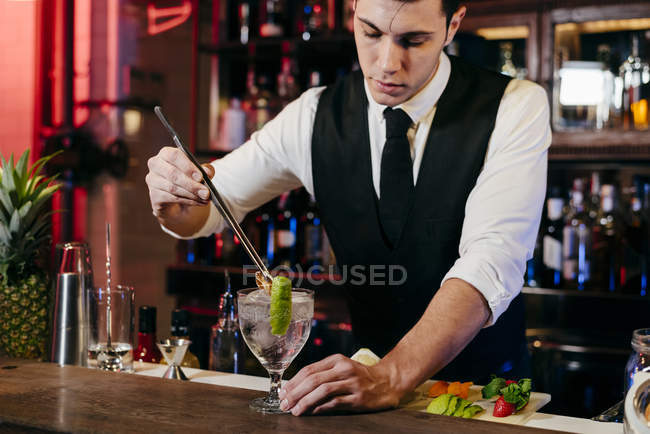 Giovane elegante barman che lavora dietro un bancone del bar mescolando bevande con frutta — Foto stock