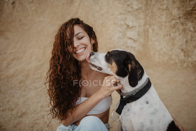 Lustiger Hund leckt aufgeregte junge Frau die Wange gegen verwitterte Hauswand auf der Straße — Stockfoto