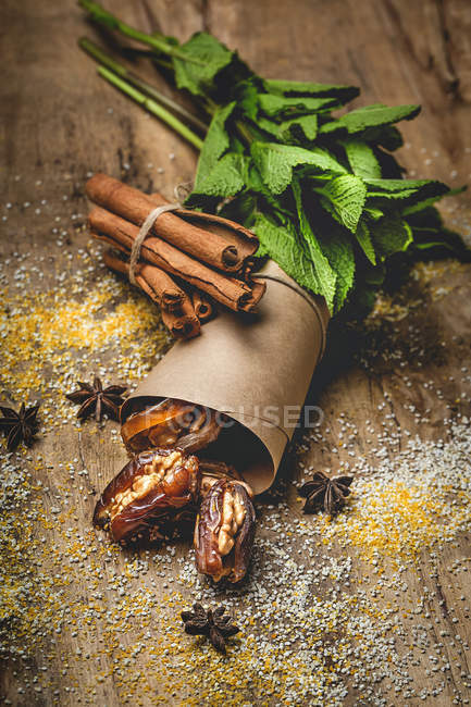 Dátiles secos, higos, menta fresca y canela para merienda halal para Ramadán envuelto en pergamino sobre mesa de madera - foto de stock