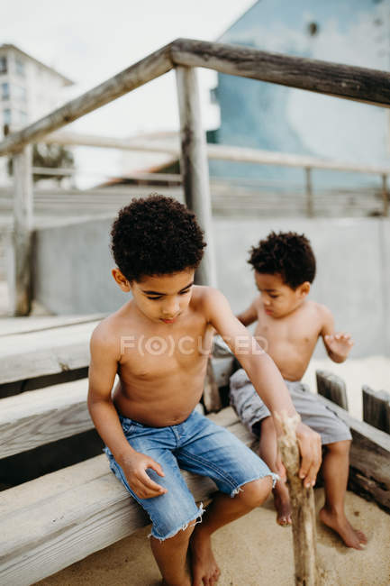 Два афроамериканских брата с палками играют вместе на песчаном берегу у моря — стоковое фото