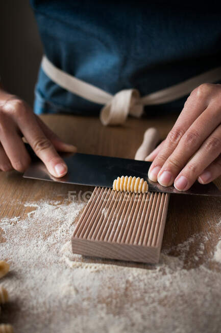 Anonymous female preparing dough for homemade gnocchetti pasta on a wooden tool in table in kitchen — Stock Photo