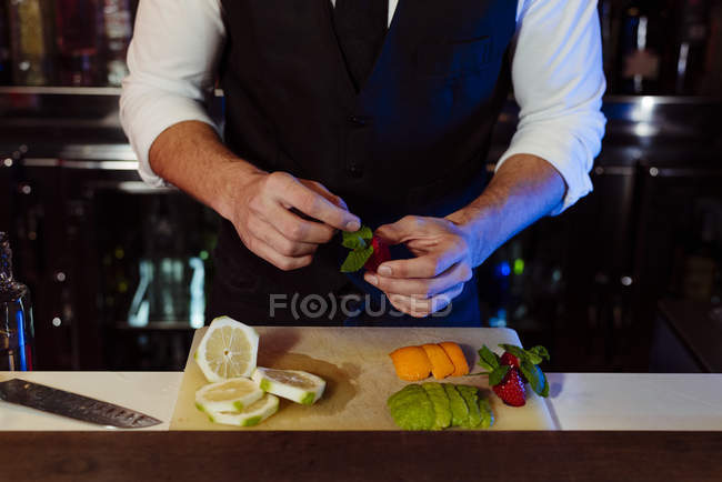Crop anônimo jovem barman elegante trabalhando atrás de um balcão de bar preparando frutas para bebidas de coquetel — Fotografia de Stock